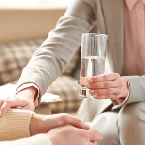 A counsellor and client sitting together in a calm session, one holding a glass of water