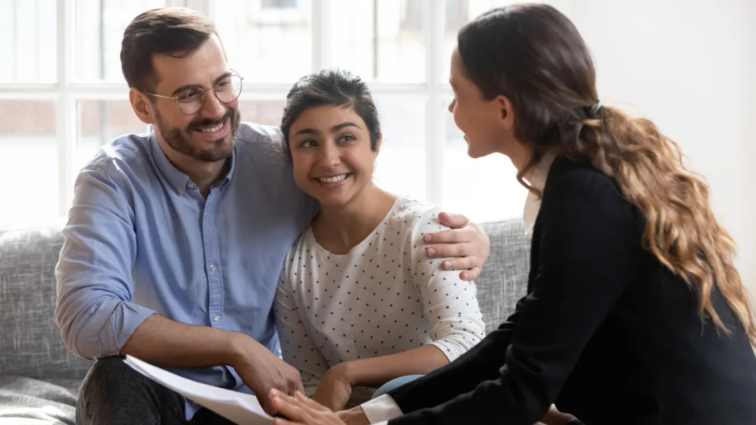 A warm couple on a sofa in conversation with a practitioner holding notes