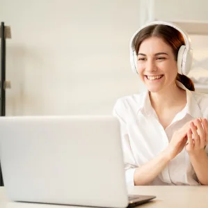 A smiling woman wearing headphones on a video call at her laptop