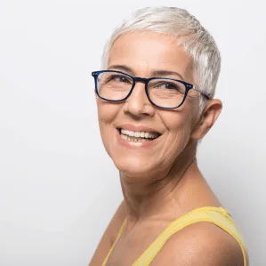 A smiling, confident woman with short grey hair and glasses against a soft light background